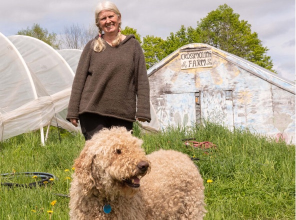 Margaret Loftus standing with her dog in front of a greenhouse at Crossmolina Farm